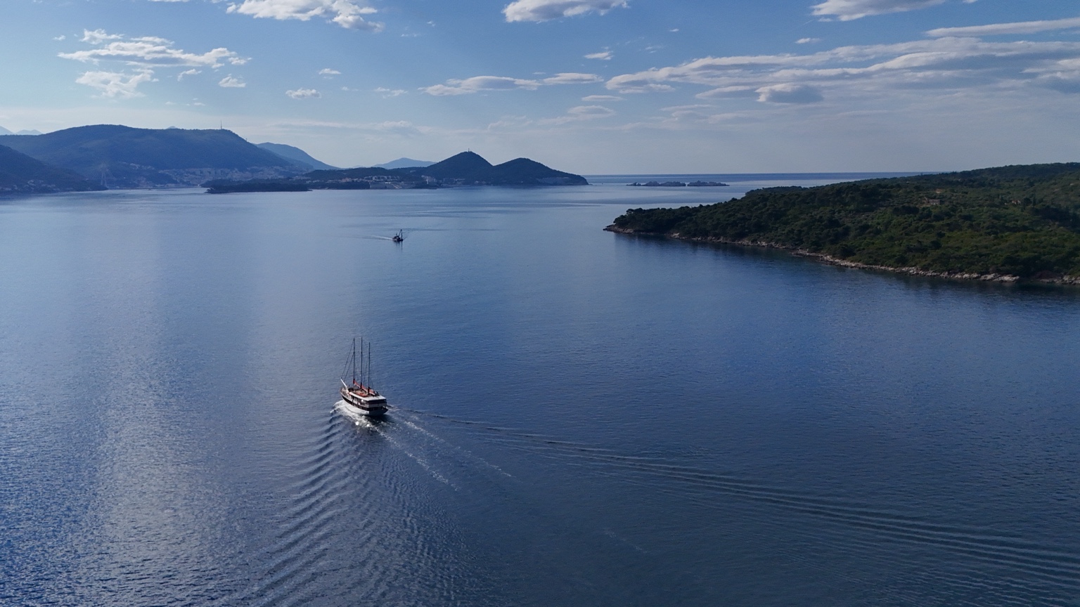A passenger boat crossing calm blue water seen from a drone above Dubrovnik