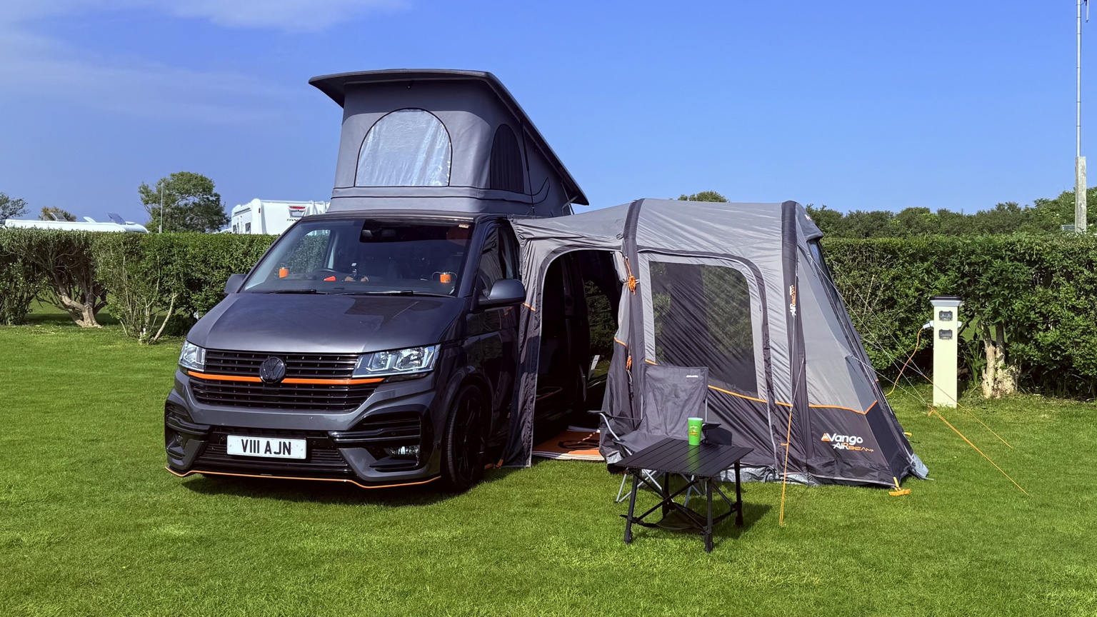 Vanilla, John's Indium Grey Volkswagen campervan, with her pop-top raised and Vango Faro Air 3 awning attached on a sunny campsite